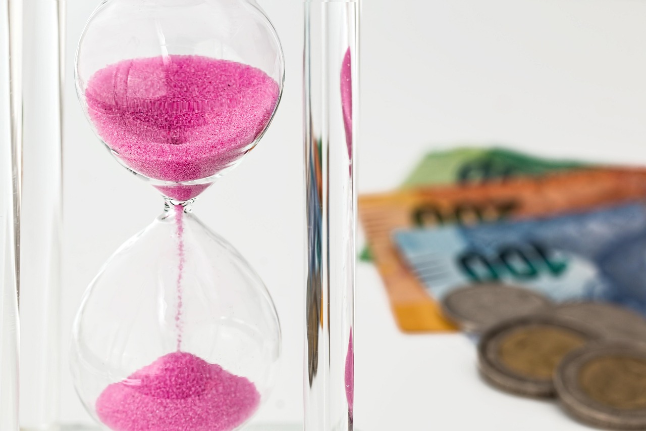 An hourglass with pink sand beside banknotes and coins